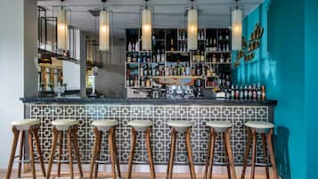 Un área de bar con un rebozo de azulejos, taburetes de madera y una variedad de botellas y vasos en estanterías.