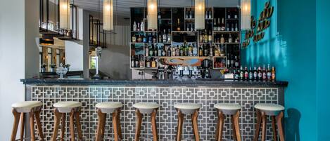 A bar area with a tiled backsplash, wooden stools, and a variety of bottles and glasses on shelves.