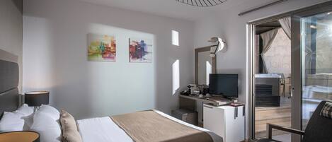 Une chambre d’hôtel moderne équipée d’un lit, d’un bureau, d’une télévision et d’un balcon avec vue.