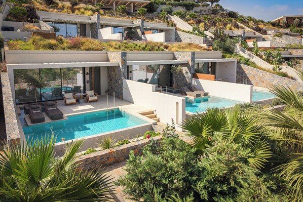 A modern resort with a large swimming pool, outdoor seating, and lush greenery. - Happy Cretan Suites (Malevizi)