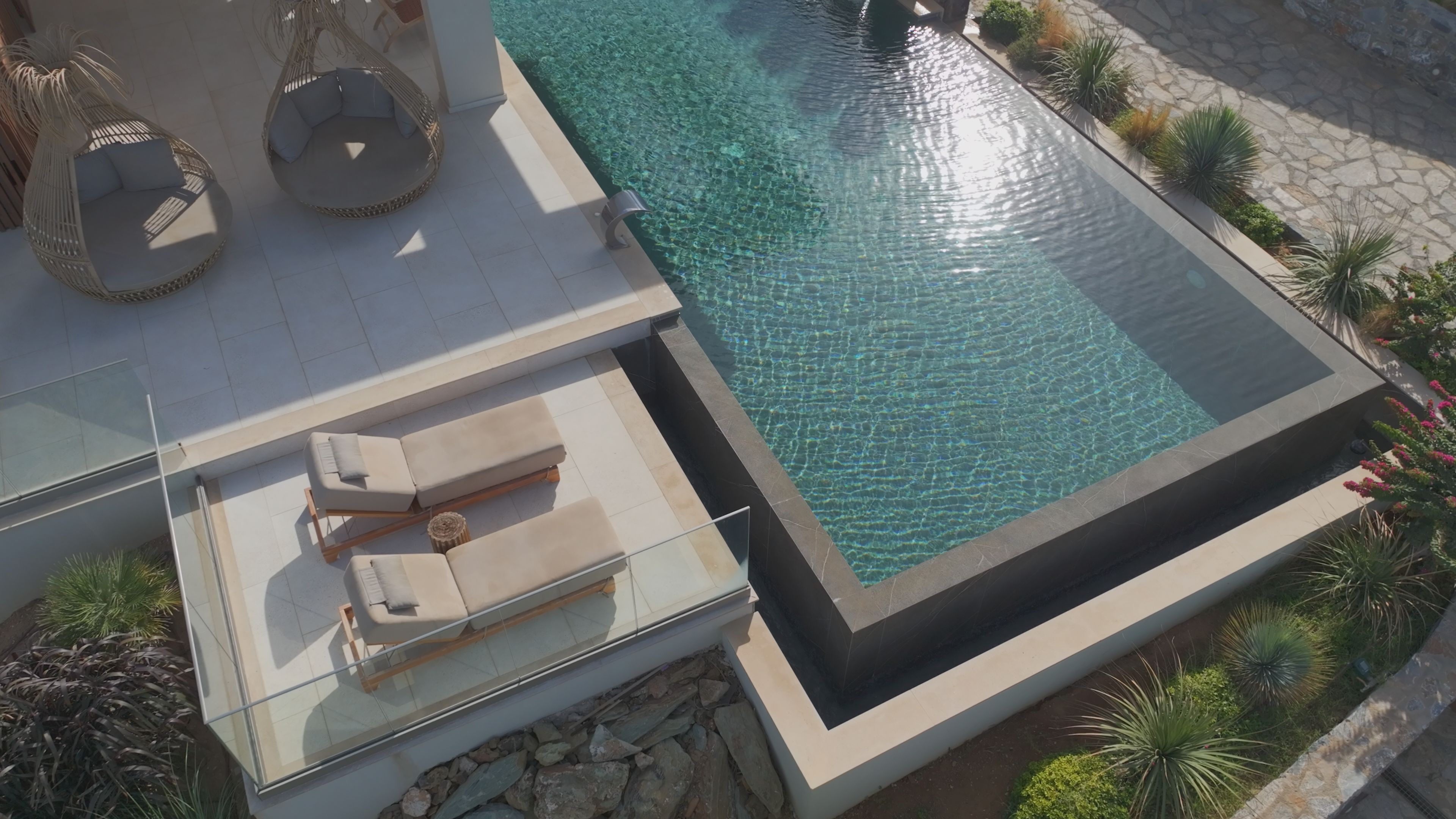 An infinity pool with clear water, surrounded by a stone deck and lush greenery.