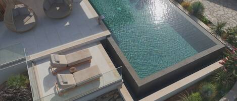 An infinity pool with clear water, surrounded by a stone deck and lush greenery.