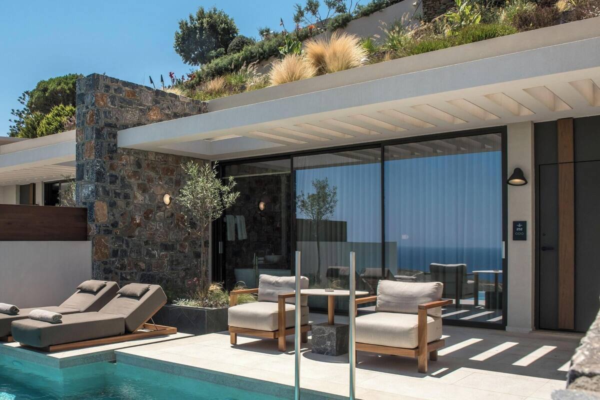 A modern poolside area with lounge chairs, a pool, and a view of the sea.