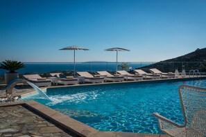 A swimming pool with lounge chairs and umbrellas, a water feature, and a view of the sea. - Happy Cretan Suites (Malevizi)