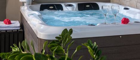 A hot tub with two glasses of water, a towel, and a flower on a table.