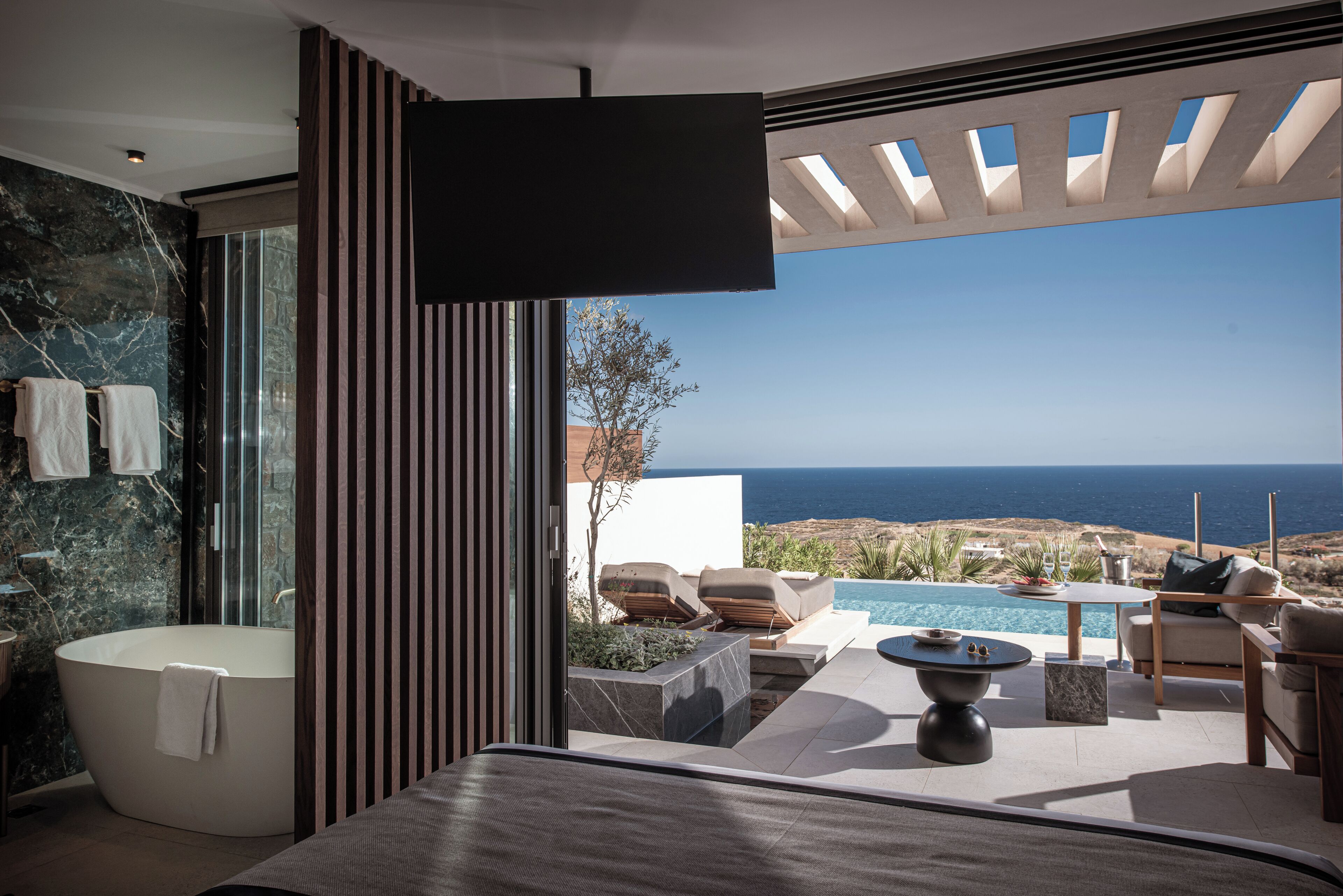 A modern bathroom with a bathtub, a shower, and a large window offering a view of the sea.