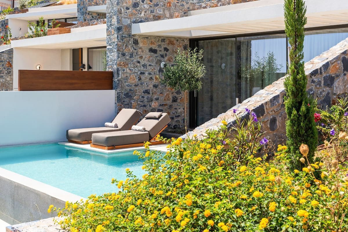 A modern poolside area with lounge chairs, a stone wall, and a view of the surrounding landscape.