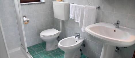 A bathroom with a toilet, bidet, and sink, tiled in light grey, with a green floor.