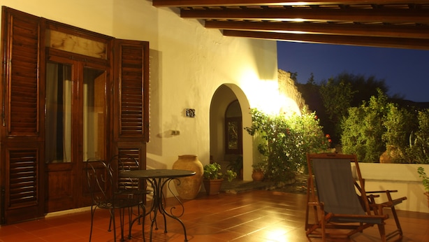 Una terrazza esterna con tavolo e sedie, una porta in legno e piante in vaso.