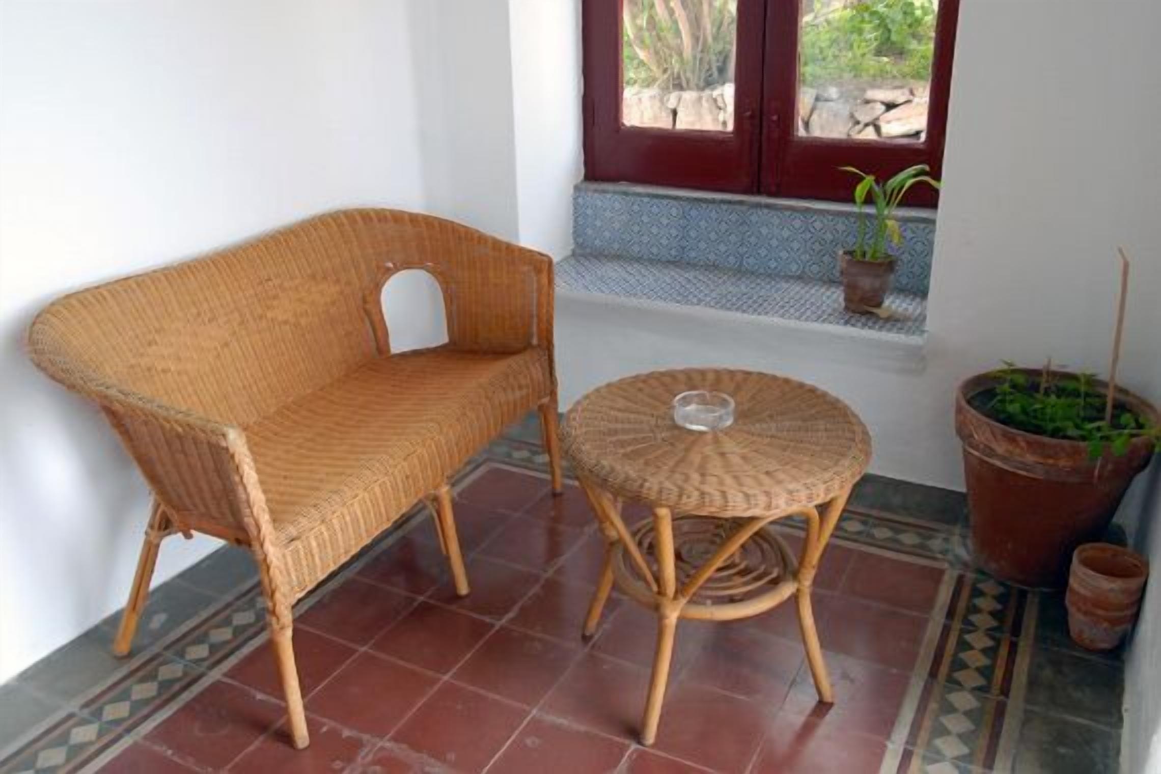 A wicker sofa and a round table in a corner with a window and potted plants.