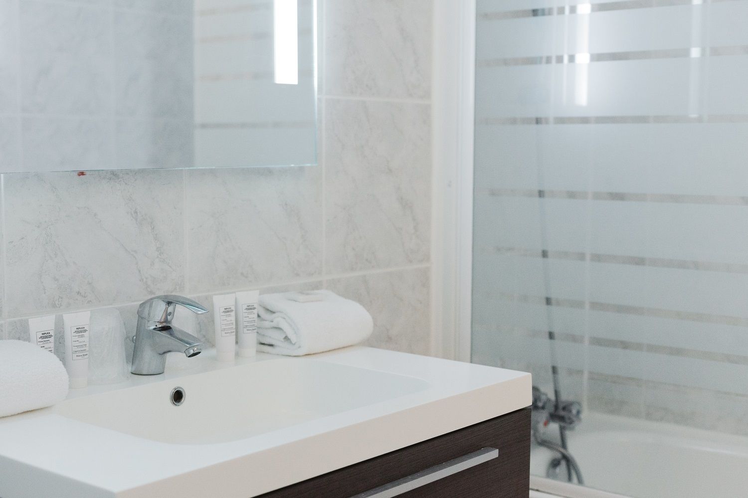 A modern bathroom with a white sink, a mirror, and a shower area with a glass door.