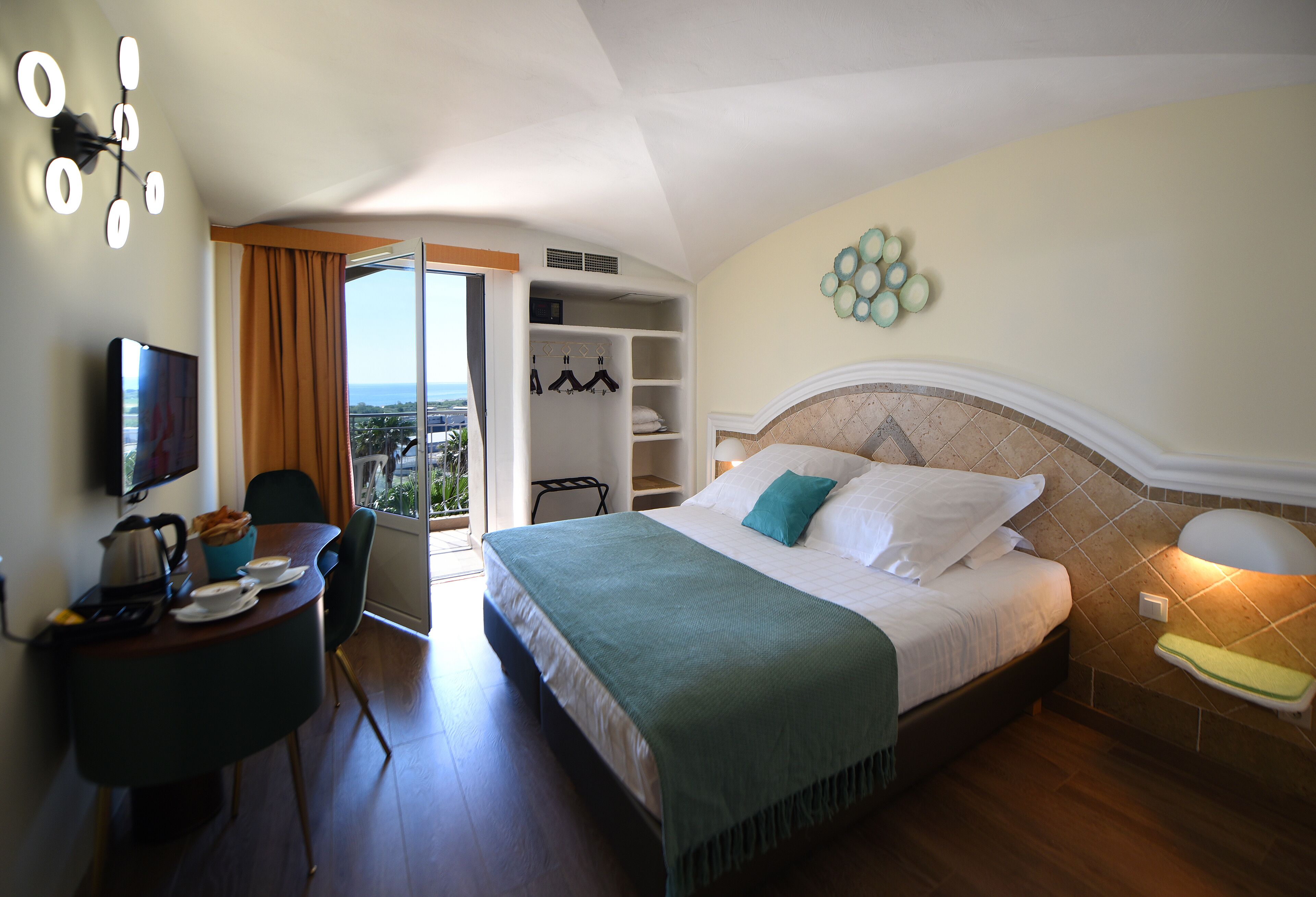 Habitación de hotel con cama, escritorio con tetera y tazas, televisión, armario y vista a la ciudad.
