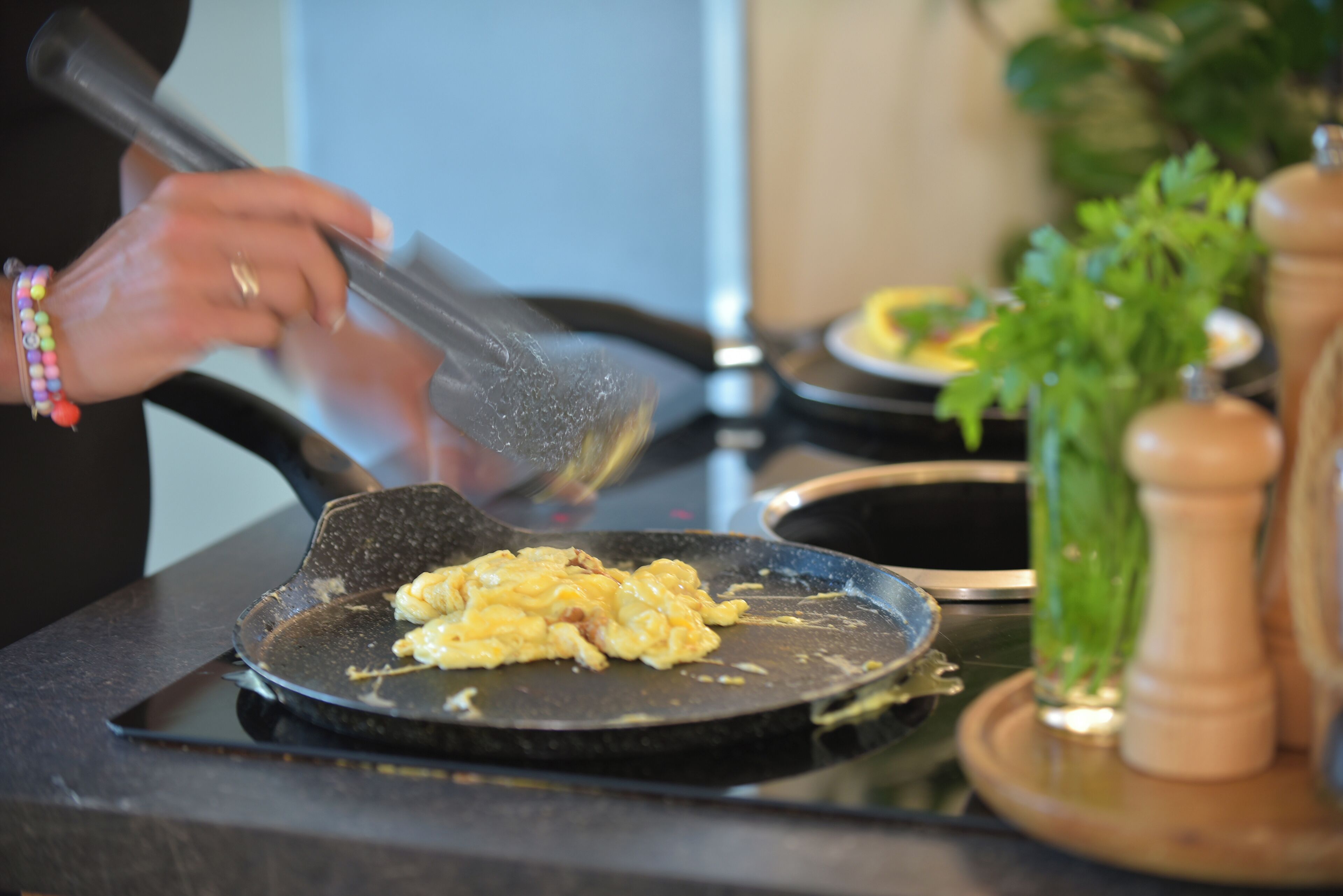 Une personne prépare des œufs brouillés dans une poêle noire sur une cuisinière.