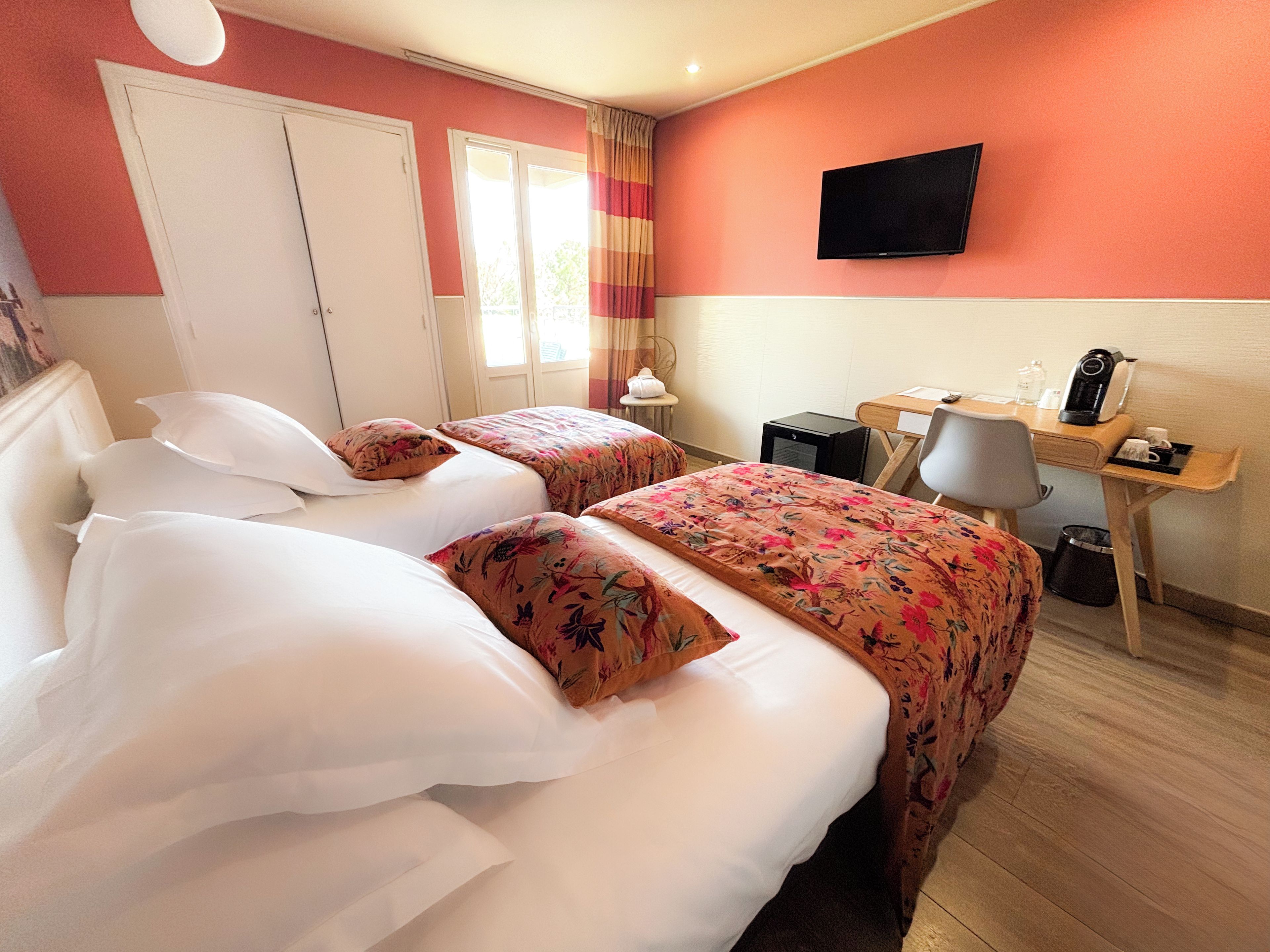 Habitación de hotel con dos camas, un escritorio, una silla, un televisor y una ventana con cortinas.