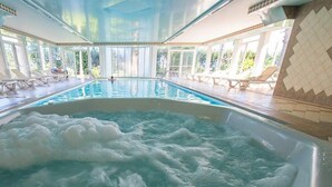 An indoor swimming pool with a hot tub, sun loungers, and a view of greenery outside. - Hôtel Spa Restaurant l'Ostella (Bastia)
