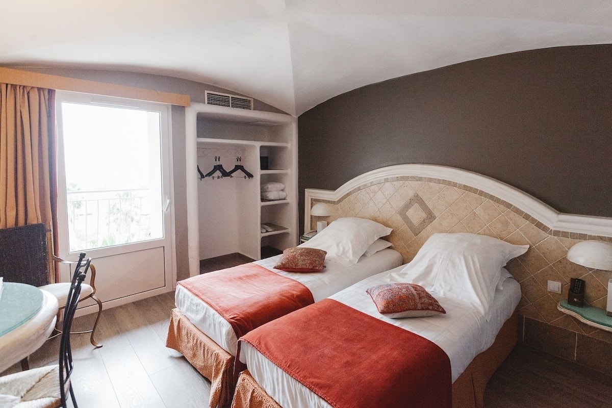 A hotel room with two beds, a wardrobe, a desk, and a window with curtains.