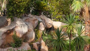 A naturalistic garden with a water feature, large rocks, and various tropical plants.