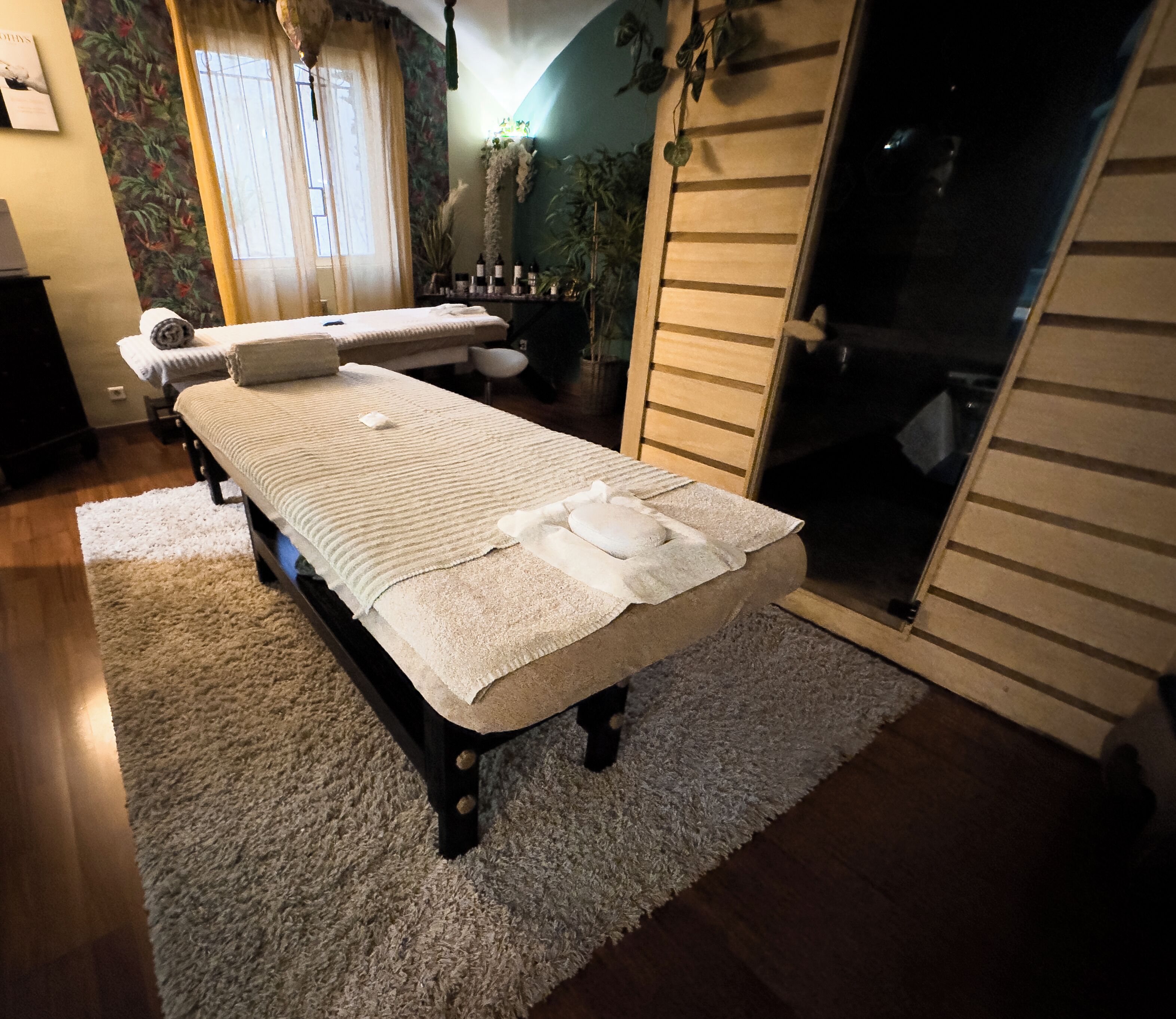 A massage table with towels and bottles, a wooden chair, and a window with curtains.