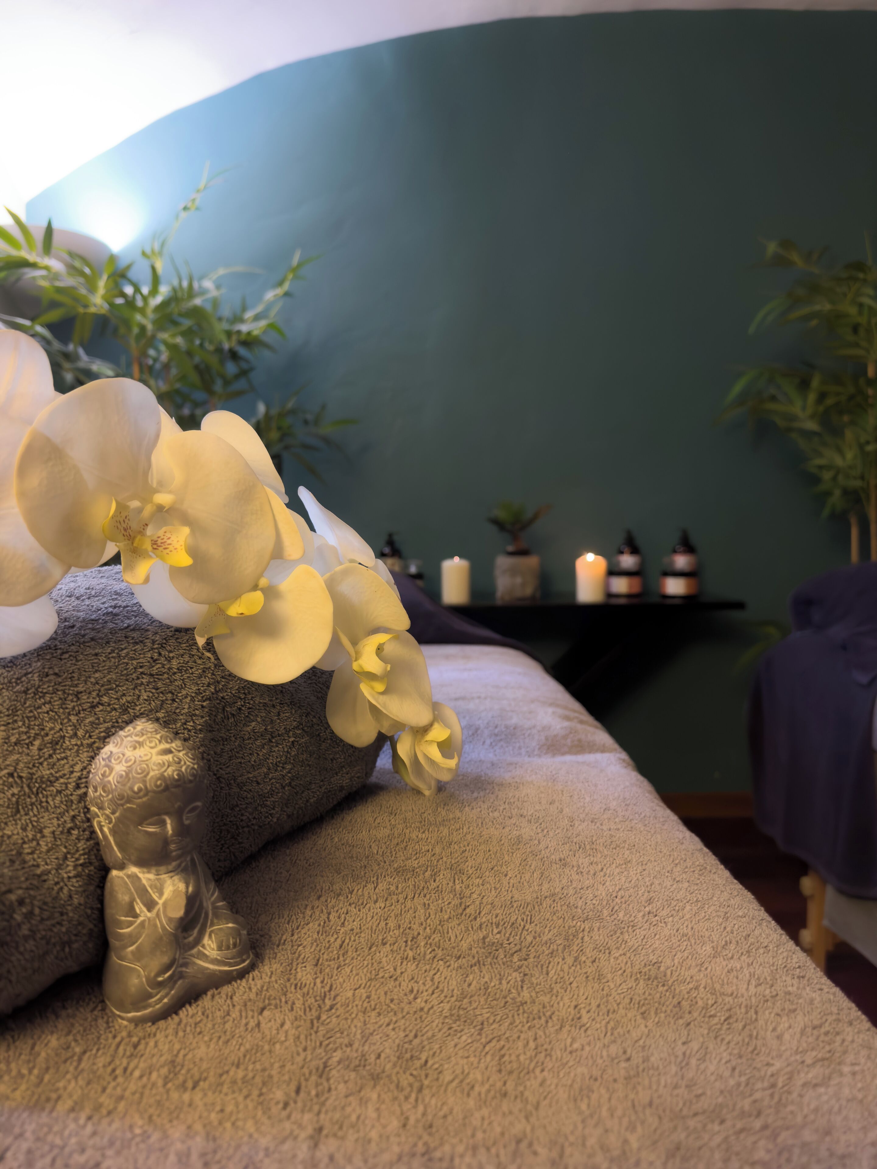 Un cuarto de spa con una camilla de masaje, una estatua de Buda y un ramo de orquídeas.