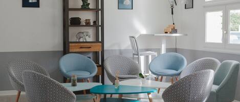 Una habitación moderna con una mesa de centro color turquesa, sillones azul claro y una estantería de madera con objetos decorativos.