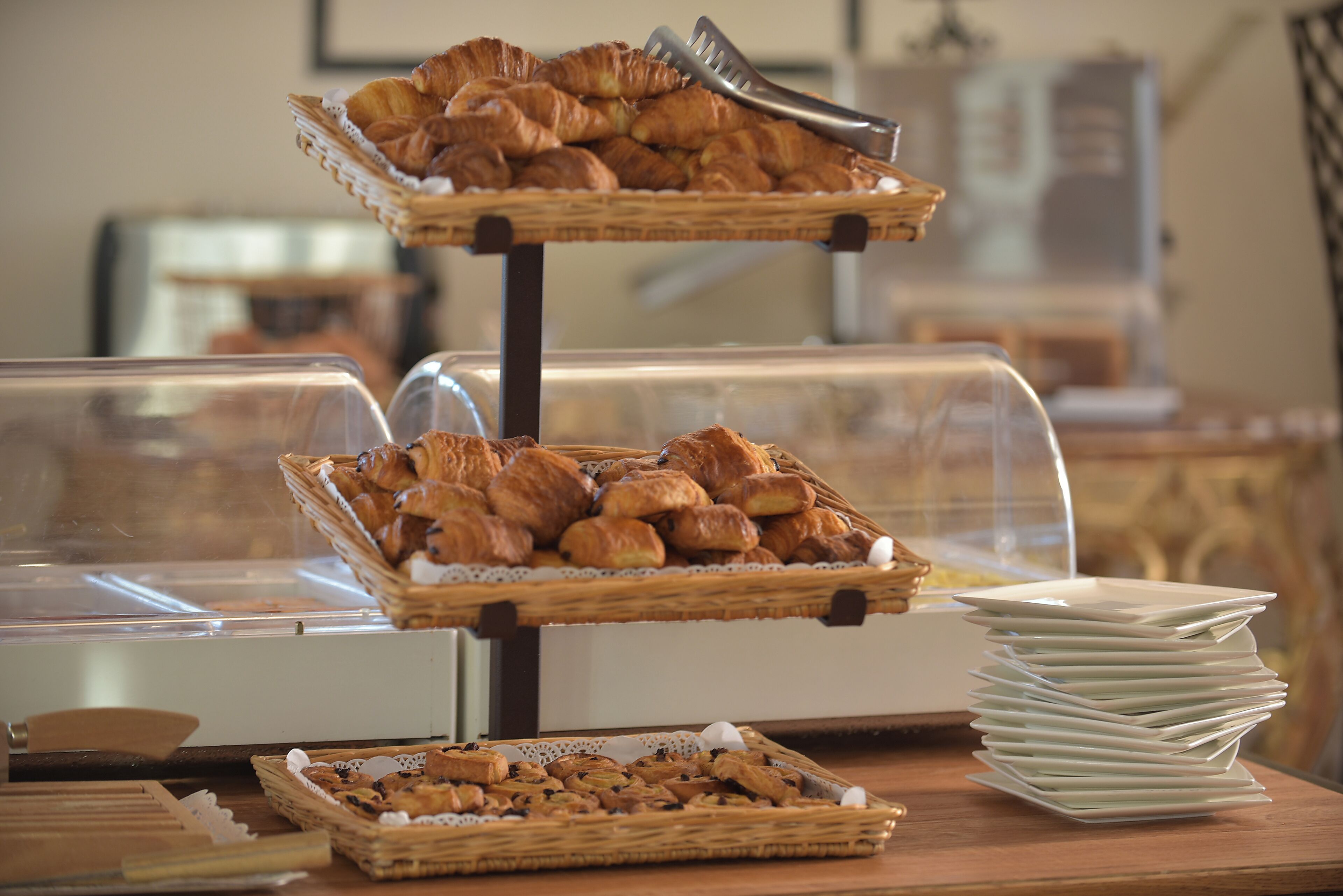 Un buffet proposant une variété de produits de boulangerie présentés dans des paniers, ainsi qu’une pile d’assiettes blanches.