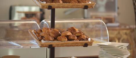Un buffet proposant une variété de produits de boulangerie présentés dans des paniers, ainsi qu’une pile d’assiettes blanches.