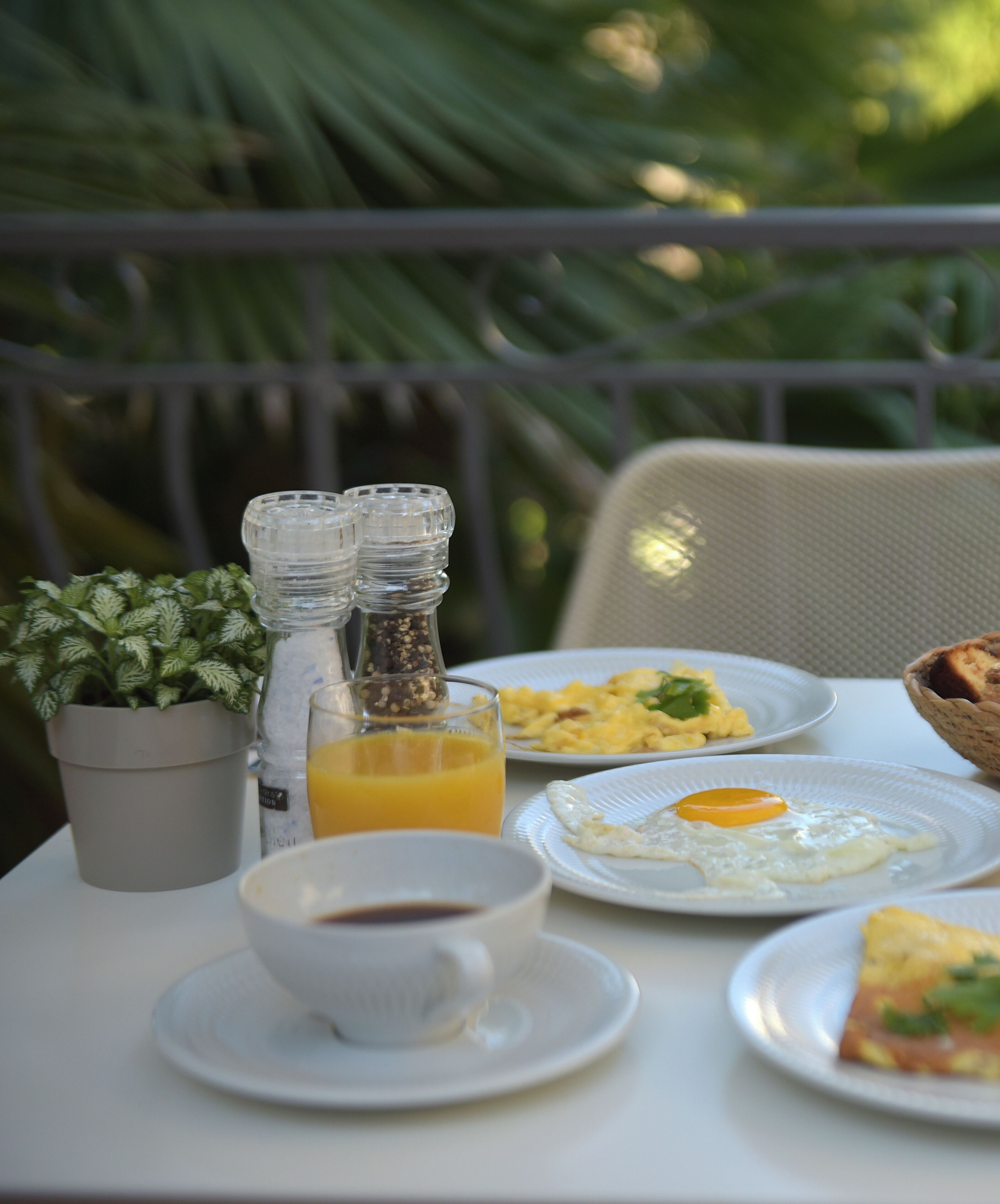 Une table dressée pour le petit-déjeuner, avec des œufs, des toasts et du jus d’orange, ainsi qu’une plante en pot et des salières et poivrières sur un balcon.