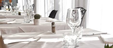 Una mesa lista para comer, con cristalería transparente, un cactus y un salero.