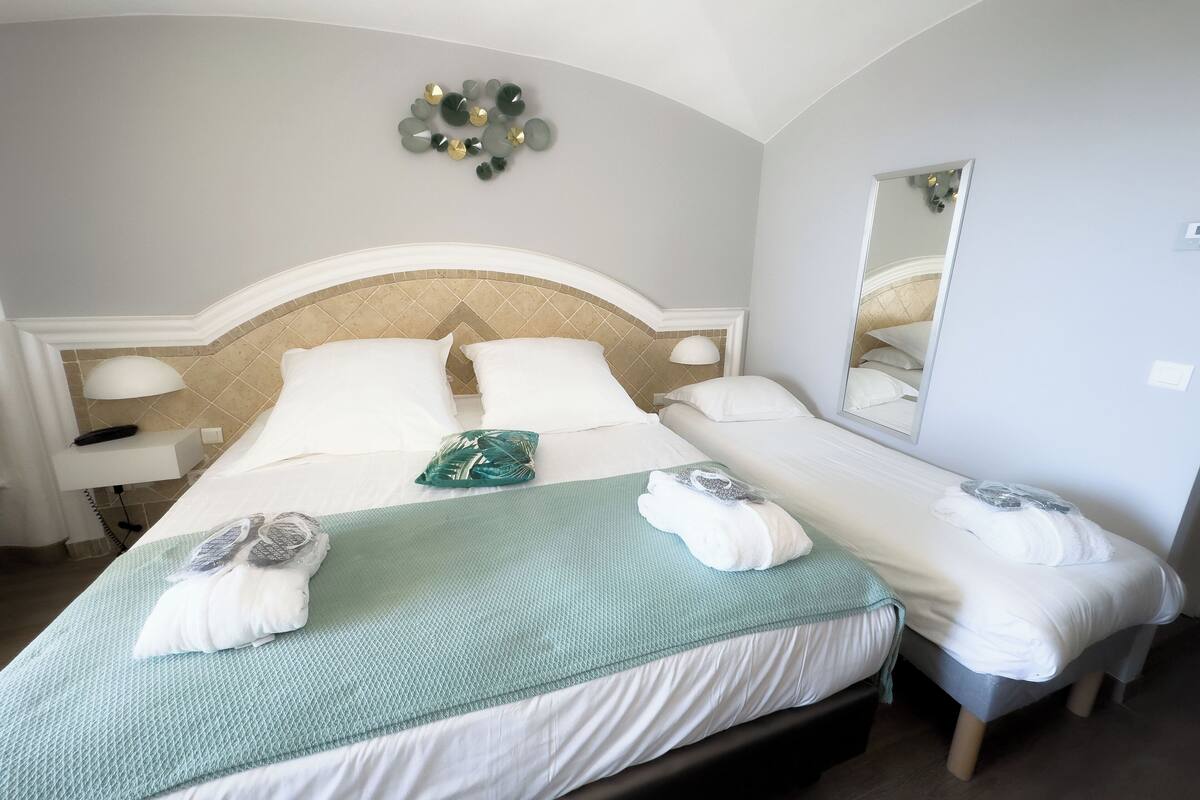 A hotel room with a large bed, a smaller bed, a mirror, and a wall decoration.