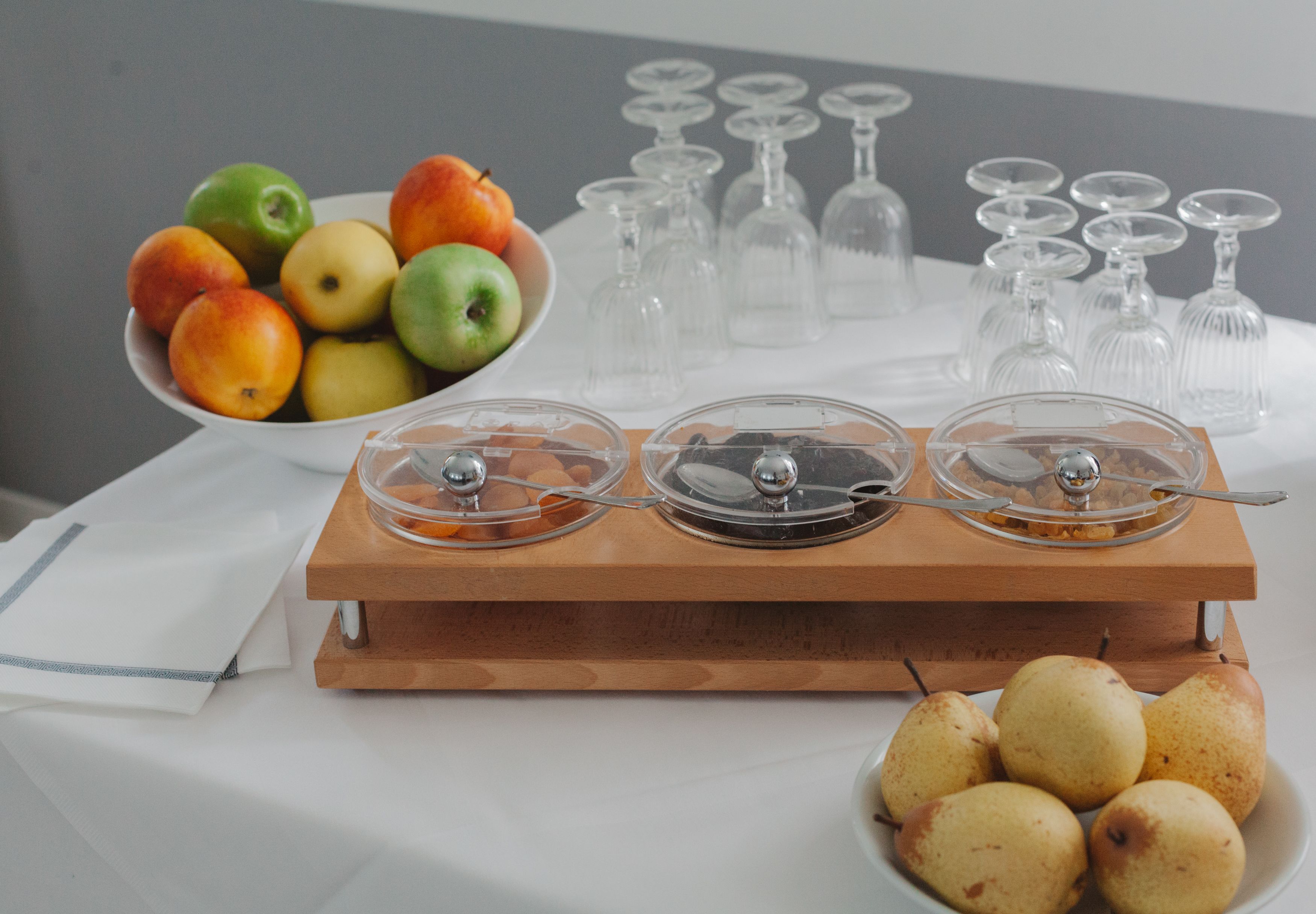 Una mesa de buffet con un bol de fruta, una tabla de madera con recipientes cubiertos y un plato de peras.