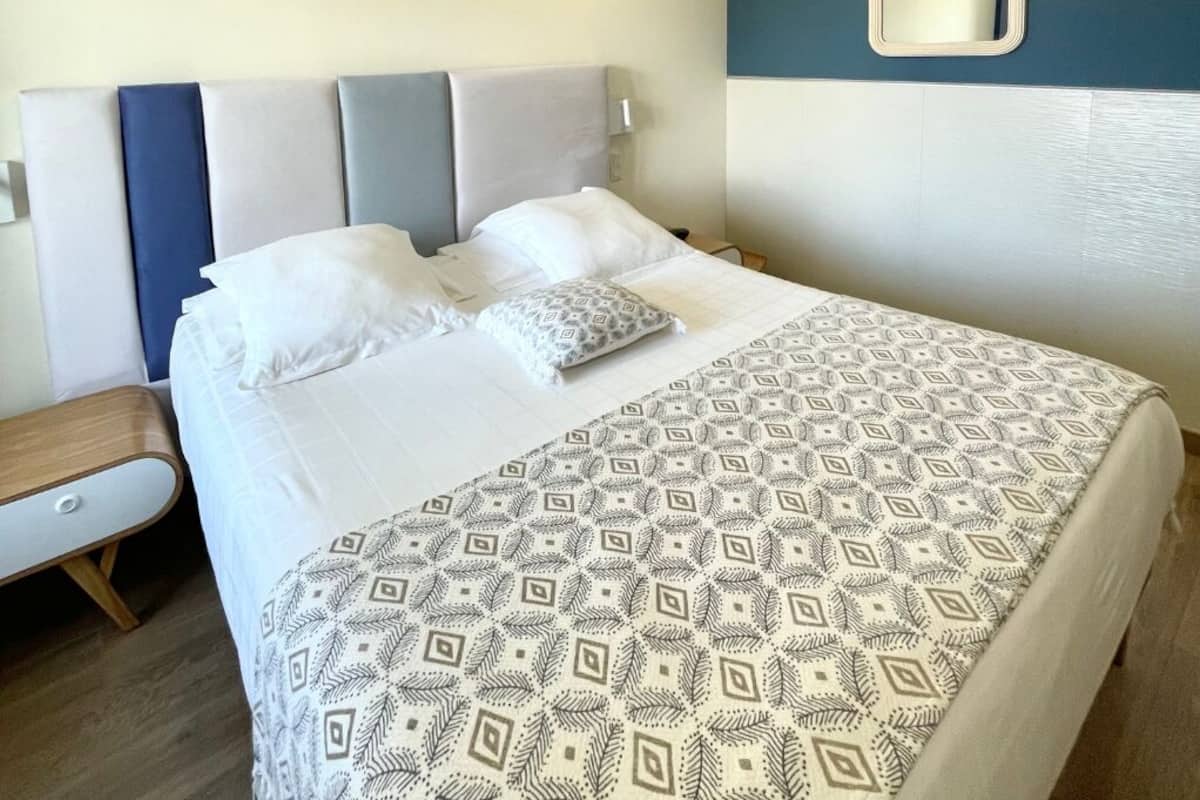 A neatly made bed with patterned bedding, a bedside table, and a wall-mounted mirror.