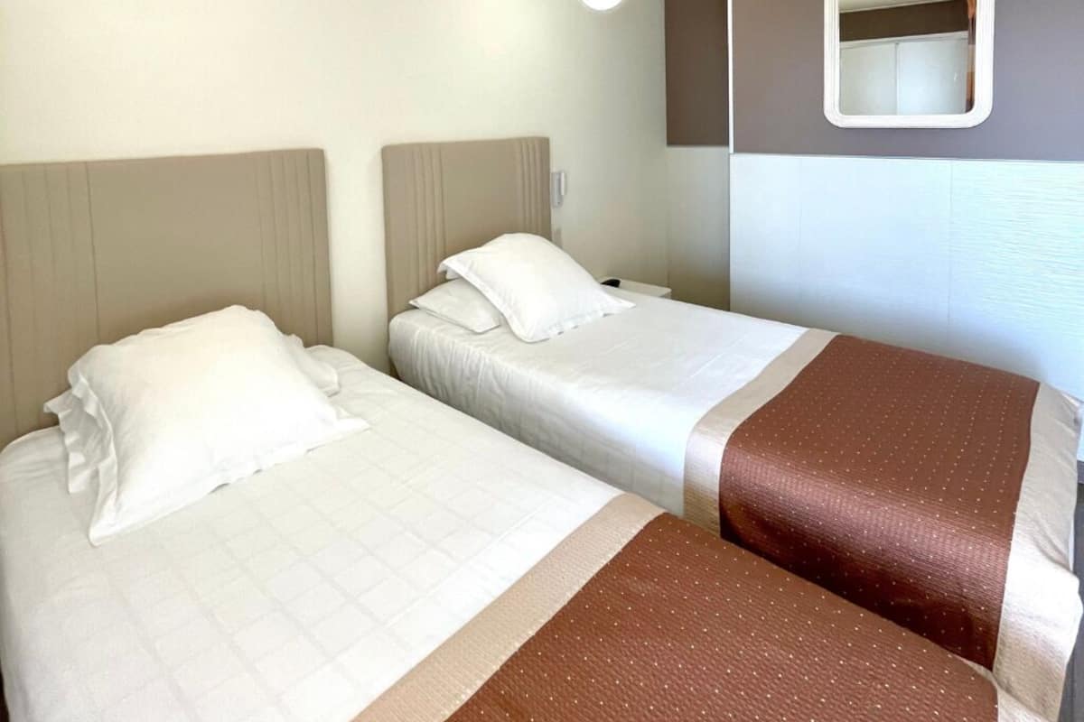 A hotel room with two beds, each with a headboard and pillows. There is a mirror on the wall and a ceiling light fixture.