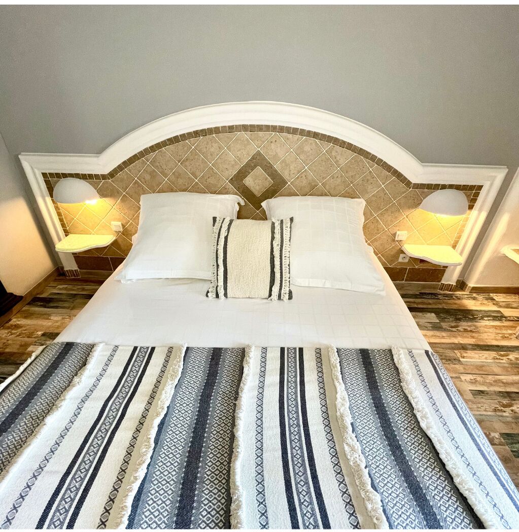 Una cama bien hecha con una colcha estampada y almohadas, un cabecero con diseño de diamantes y dos lámparas de noche.