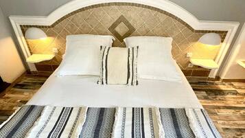 Una cama bien hecha con una colcha estampada y almohadas, un cabecero con diseño de diamantes y dos lámparas de noche.