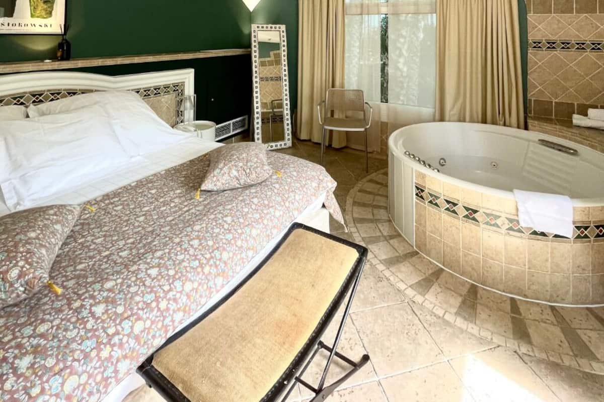 A hotel room with a large bed, a sitting area with a chair, a large bathtub, and a mirror.