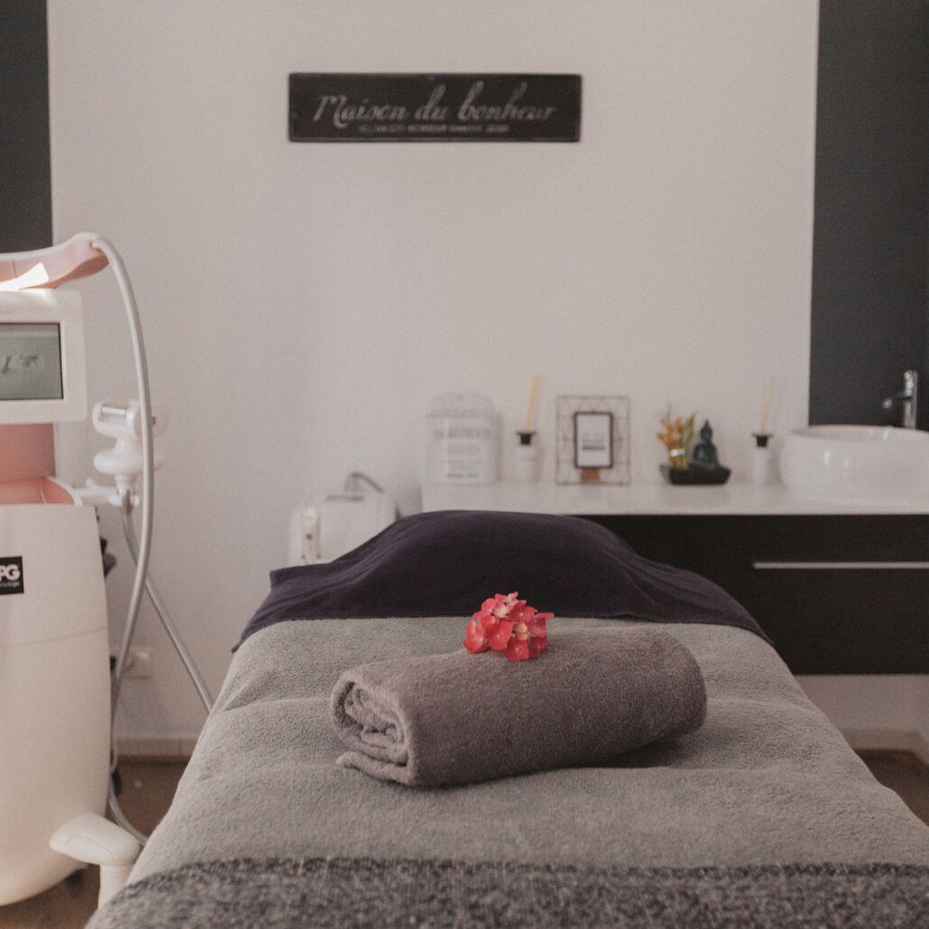 A room with a massage table, a wall-mounted sign, a white machine, and a small statue.