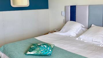 A hotel room with a bed, a bedside table, a mirror, and a wall-mounted light fixture.