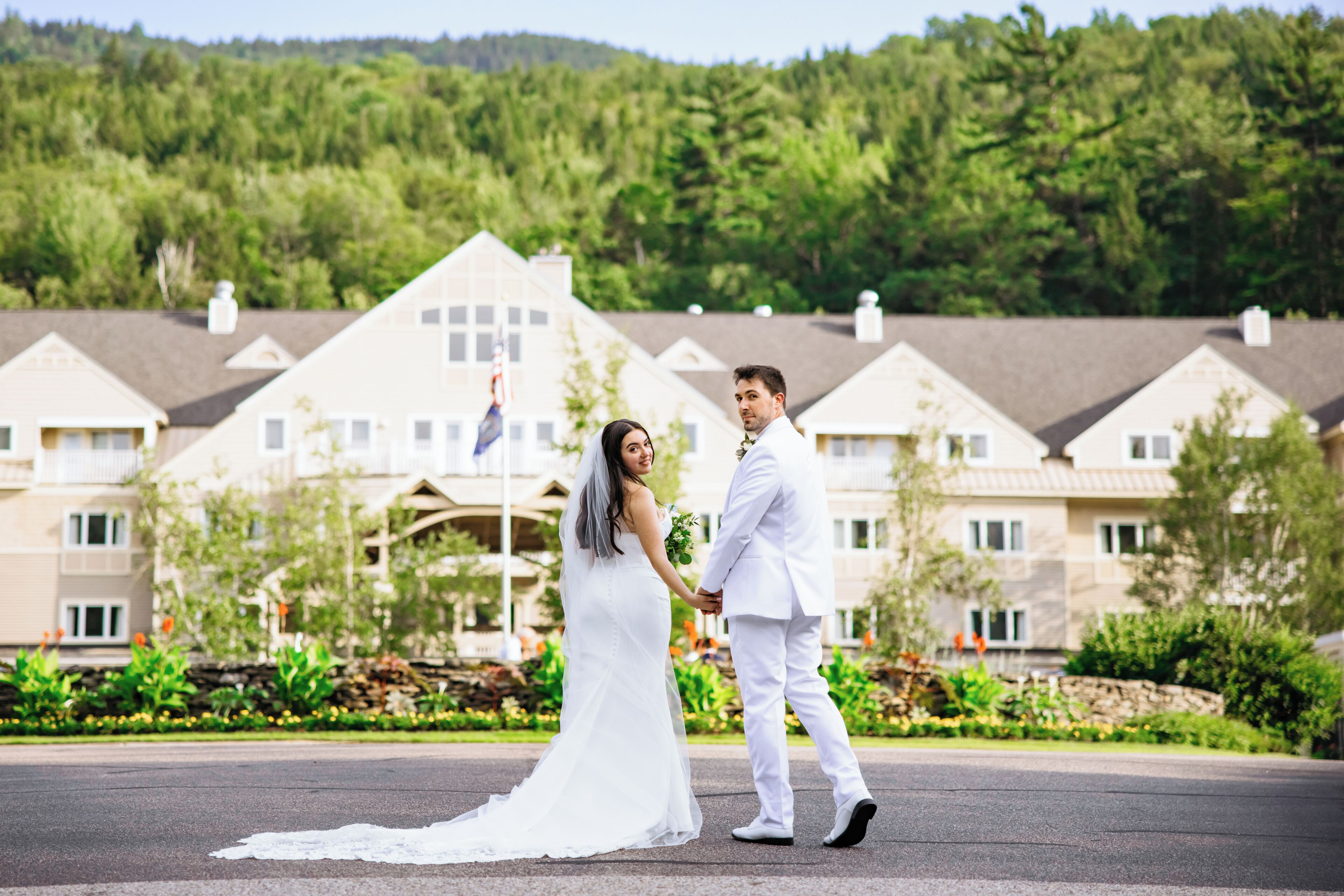 A couple in wedding attire standing in front of a building with a landscaped garden.