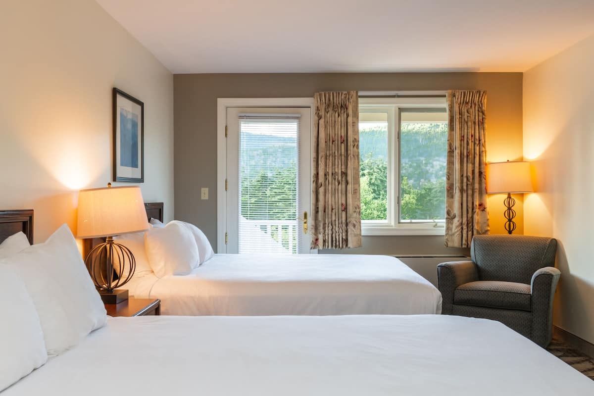 A hotel room with two beds, a chair, a desk, and a window with curtains.