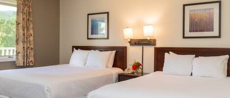 A hotel room with two beds, a nightstand with a phone and flowers, wall-mounted lamps, and framed pictures.