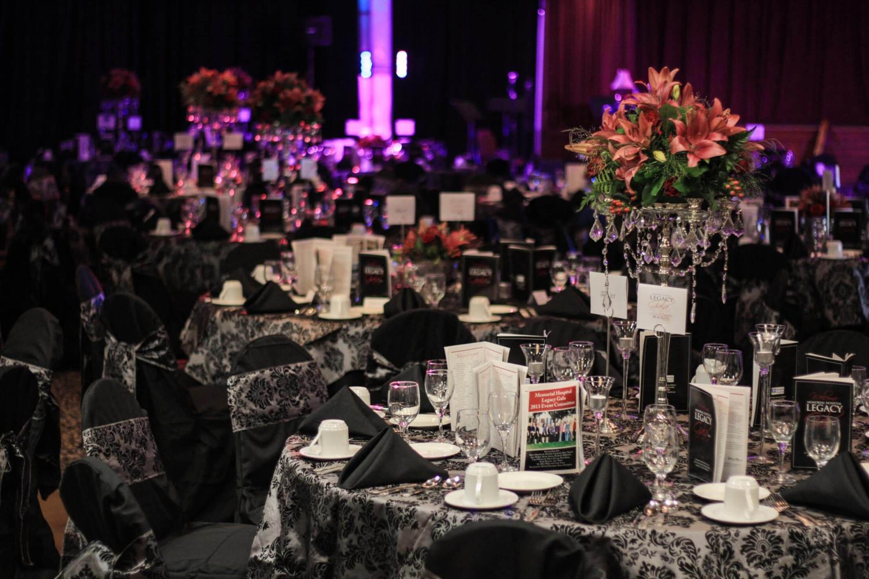 A banquet hall with tables set for a formal event, featuring black and white tablecloths, white plates, and clear glassware.