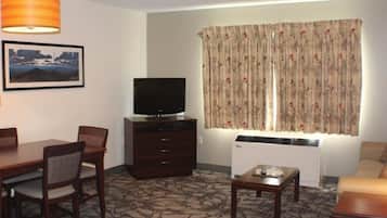 A hotel room with a dining table, chairs, a TV, a small sofa, a coffee table, and a patterned carpet.