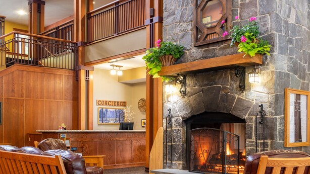 A spacious lobby with a stone fireplace, wooden furniture, and a balcony. - Grand Summit Hotel at Attitash (Bartlett)