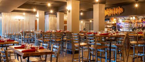 Um restaurante espaçoso com várias mesas e cadeiras, área de bar e um design de teto moderno.