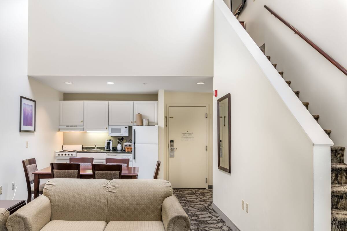 A hotel room with a kitchenette, a dining area with a table and chairs, and a staircase.