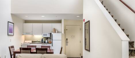 A hotel room with a kitchenette, a dining area with a table and chairs, and a staircase.