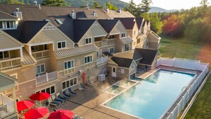 A multi-story hotel with a swimming pool, outdoor seating, and a view of the surrounding hills. - Grand Summit Hotel at Attitash (Bartlett)