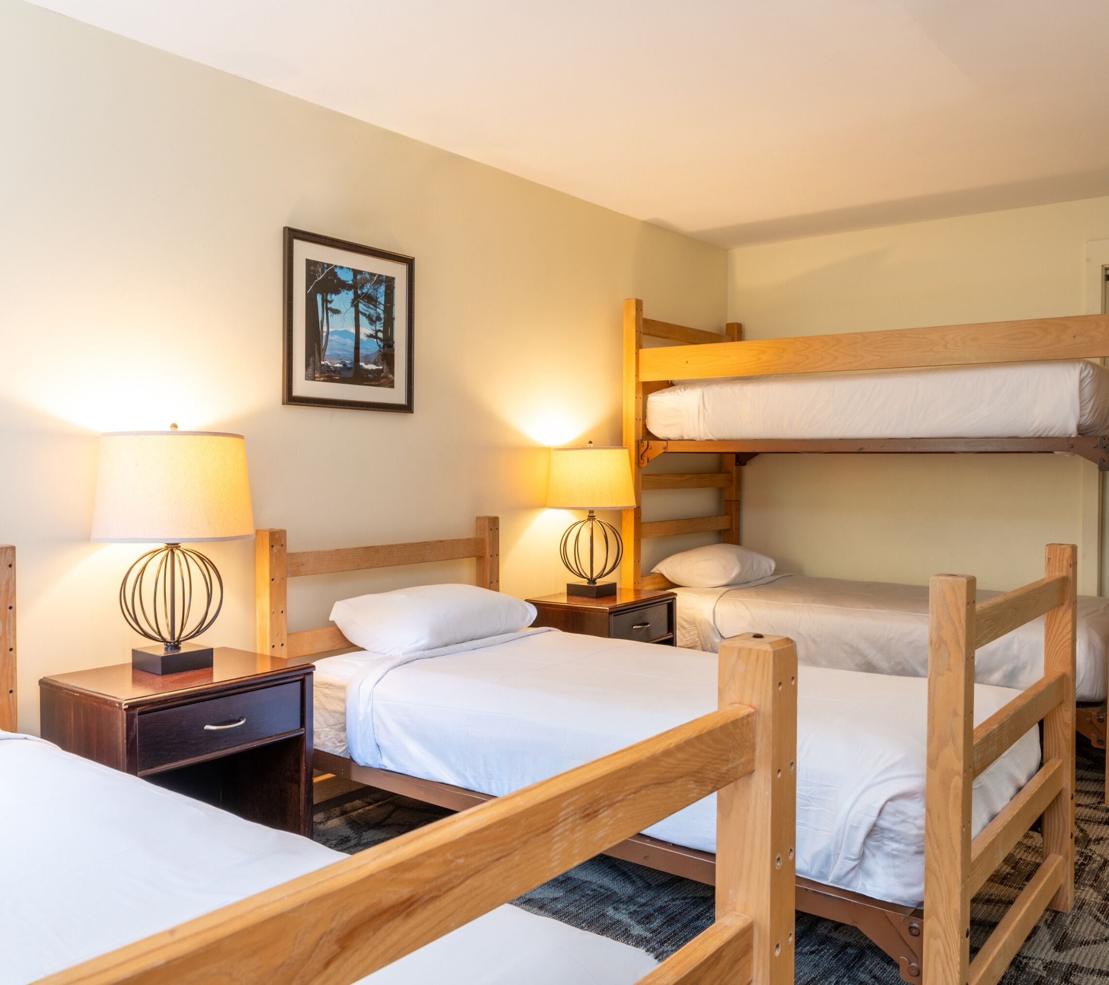 A hotel room with bunk beds, two bedside tables with lamps, a framed picture on the wall, and a carpeted floor.