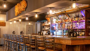 A bar area with wooden chairs, a bar counter with bottles, and a hanging light fixture. - Grand Summit Hotel at Attitash (Bartlett)