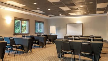 Un salón de conferencias con una mesa grande, sillas, una pantalla de proyector y ventanas que dan a zonas verdes.